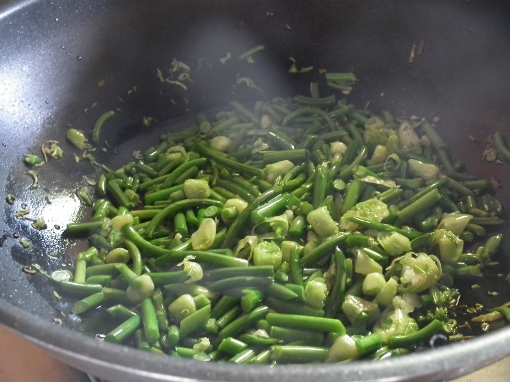 Cooking garlic scapes by frying in a wok at Tree House Kitchen.