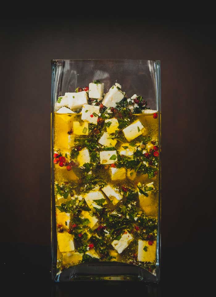 Garlicky marinated feta cheese in a tall glass dish.