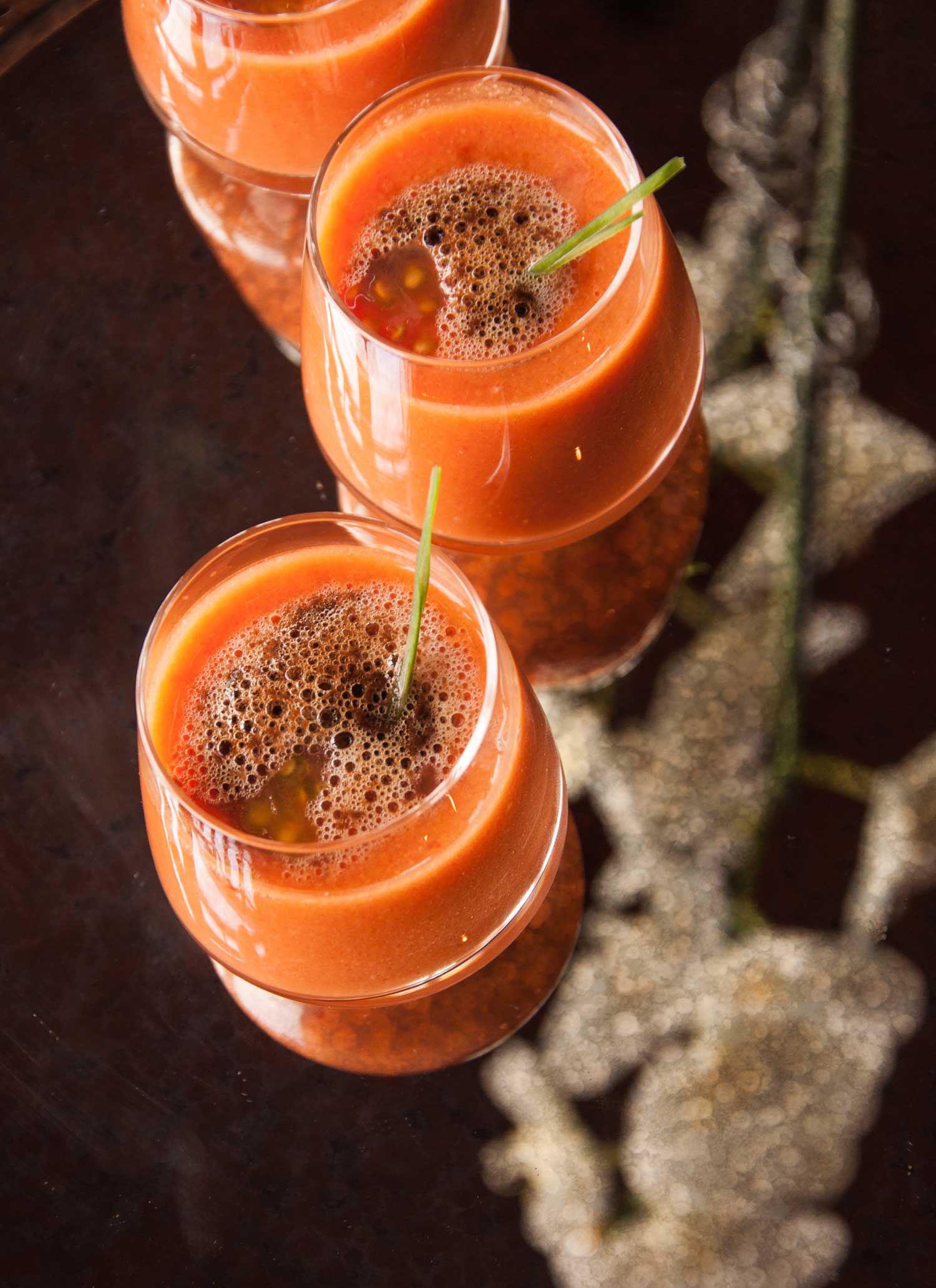 Bright orange vegetable gazpacho soup in small glasses, topped with black olive foam and fresh chives.  