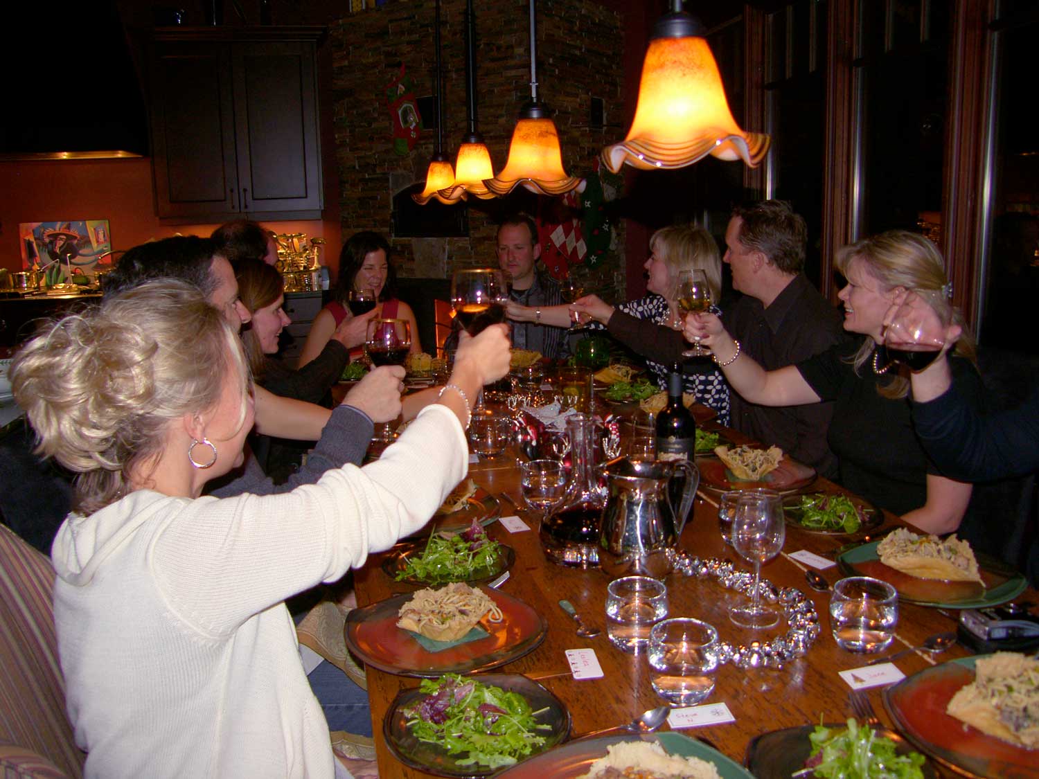 A group cheers and clinks their wine glasses together over the dinner table.